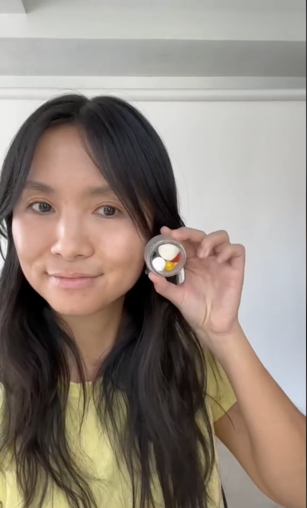 a woman holding up a jar of unmixed pigments to her face and smiling at the camera